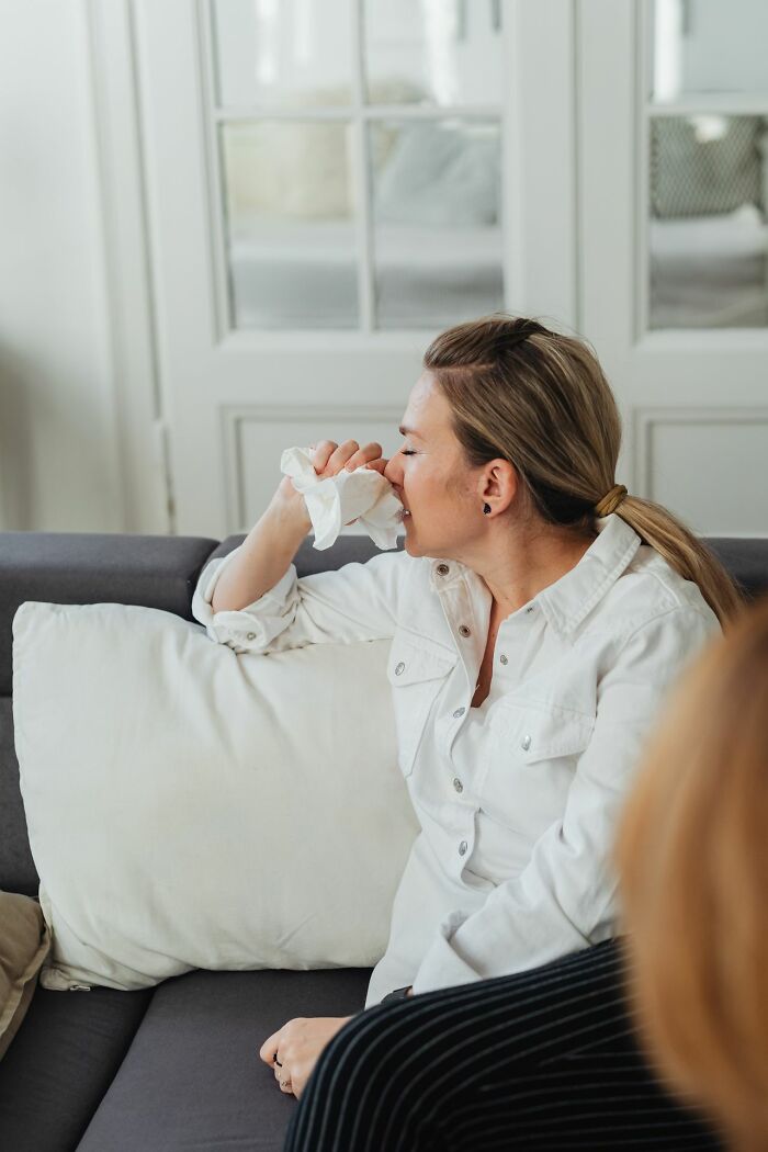 A woman on a gray couch wiping her nose with a tissue, sharing one of the rarest things that happened.
