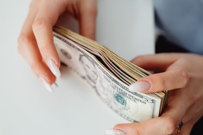 A woman is counting a stack of US dollar bills, likely her inheritance or part of it, relating to a great-grandma's will. A woman is counting a stack of US dollar bills, likely her inheritance or part of it, relating to a great-grandma's will.