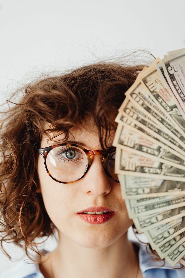 A woman with glasses holding a fan of money, depicting a fortunate event, one of the rarest things.