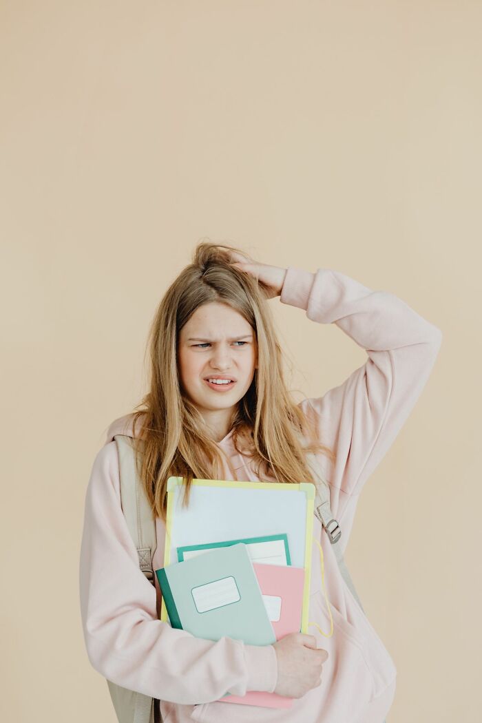 A confused young girl scratching her head while holding books, representing fascinating things about the world.