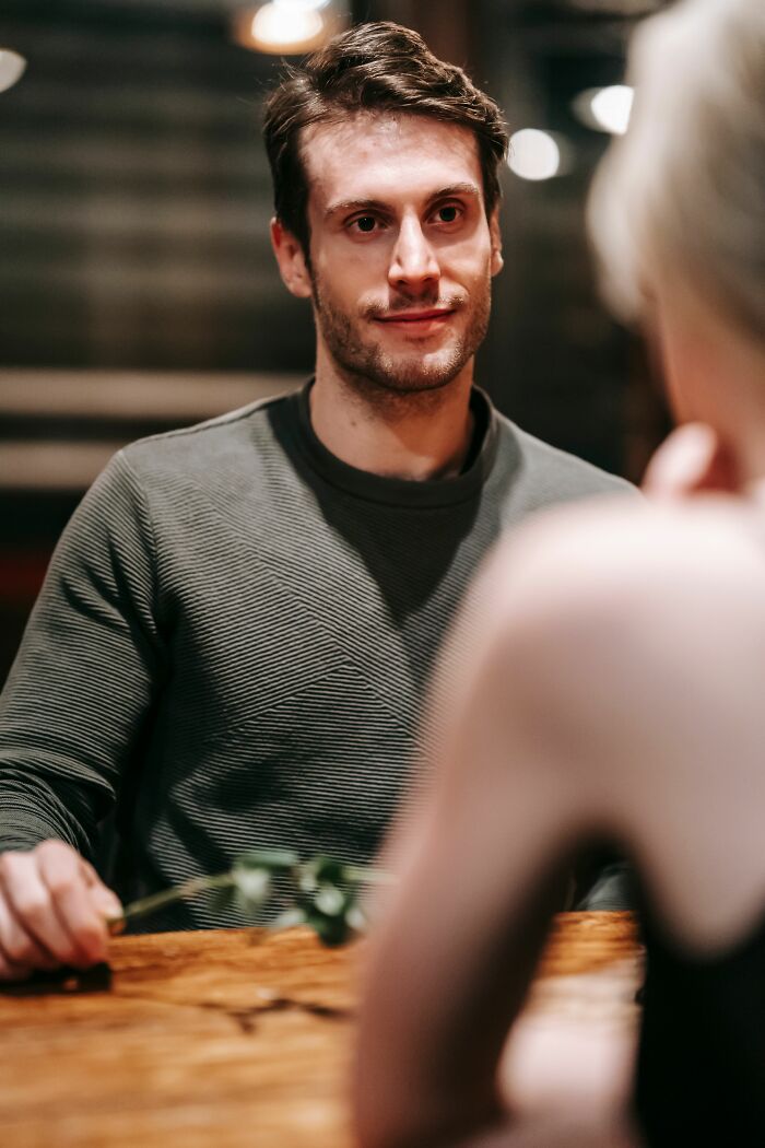 A man looks at a woman on a date, once thought perfect. He holds a rose, considering his baby talk.