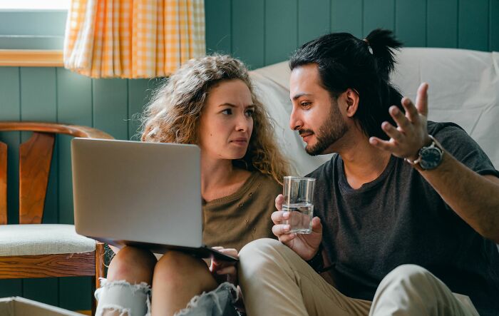 A couple looking confused while using a laptop, discussing things everyone should know before getting married.