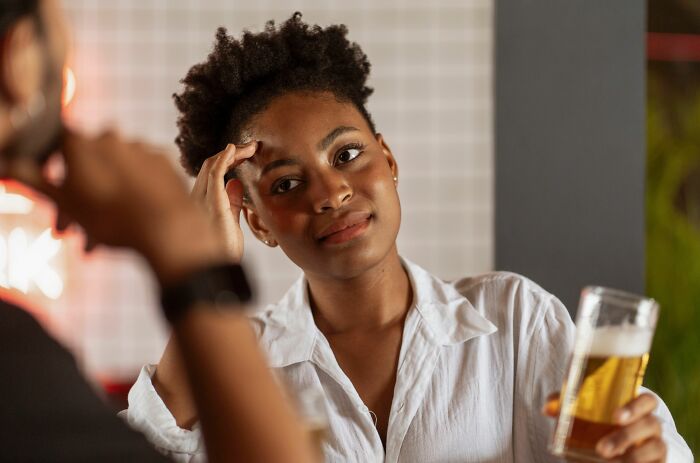 A woman with short curly hair looks over her shoulder, holding a glass of beer. This shows women changing their minds.