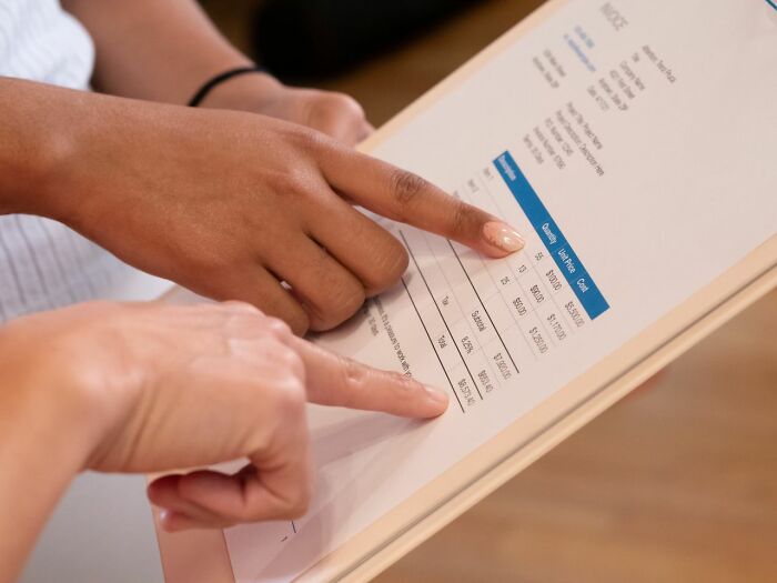 Two people pointing at a financial invoice, discussing figures, exposing behind the scenes company finances.