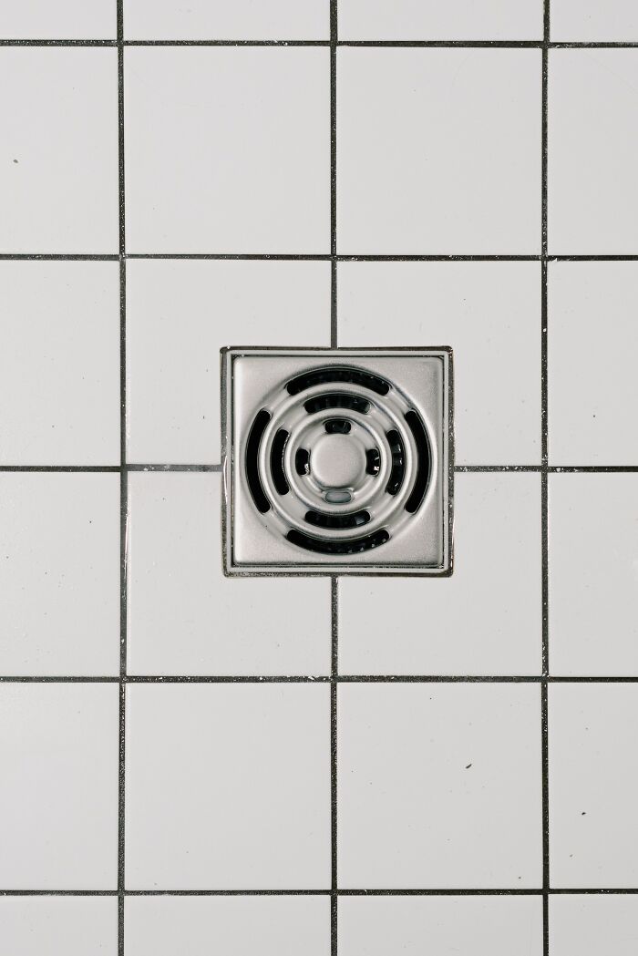 A metal shower drain on white tiled floor, a cheating red flag possibly indicating efforts to hide evidence.