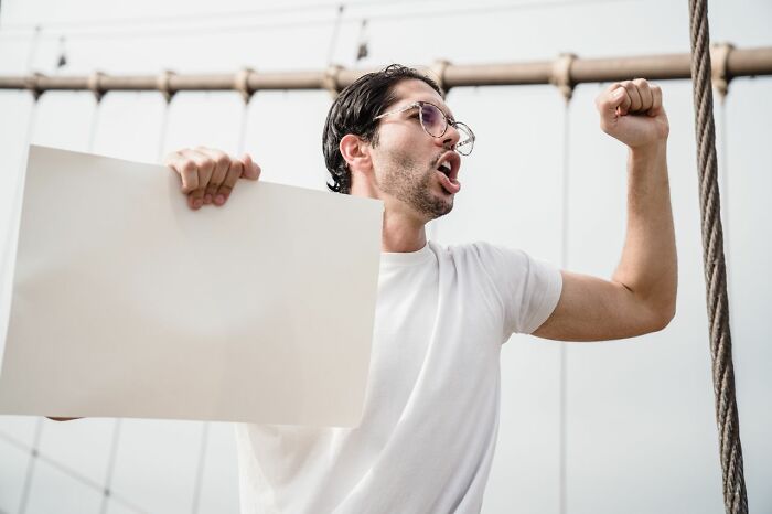 A man holding a blank sign and yelling, representing ridiculous problems HR and adults face.