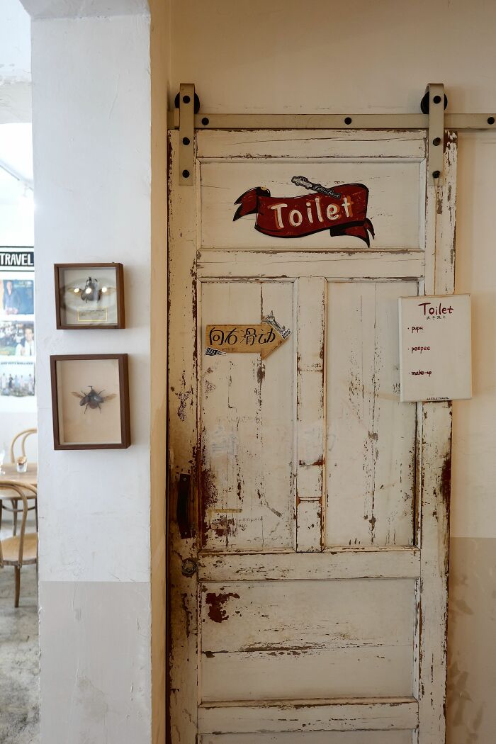 A rustic white wooden door with a 'Toilet' sign and a handwritten list, reflecting health inspections and why one would be vegetarian.