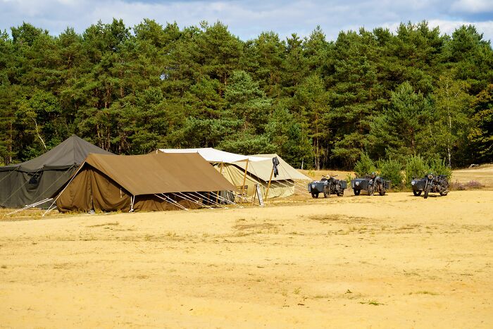 Military tents and motorcycles in a sandy area near a forest, reflecting extraordinary stories of World War II veterans.