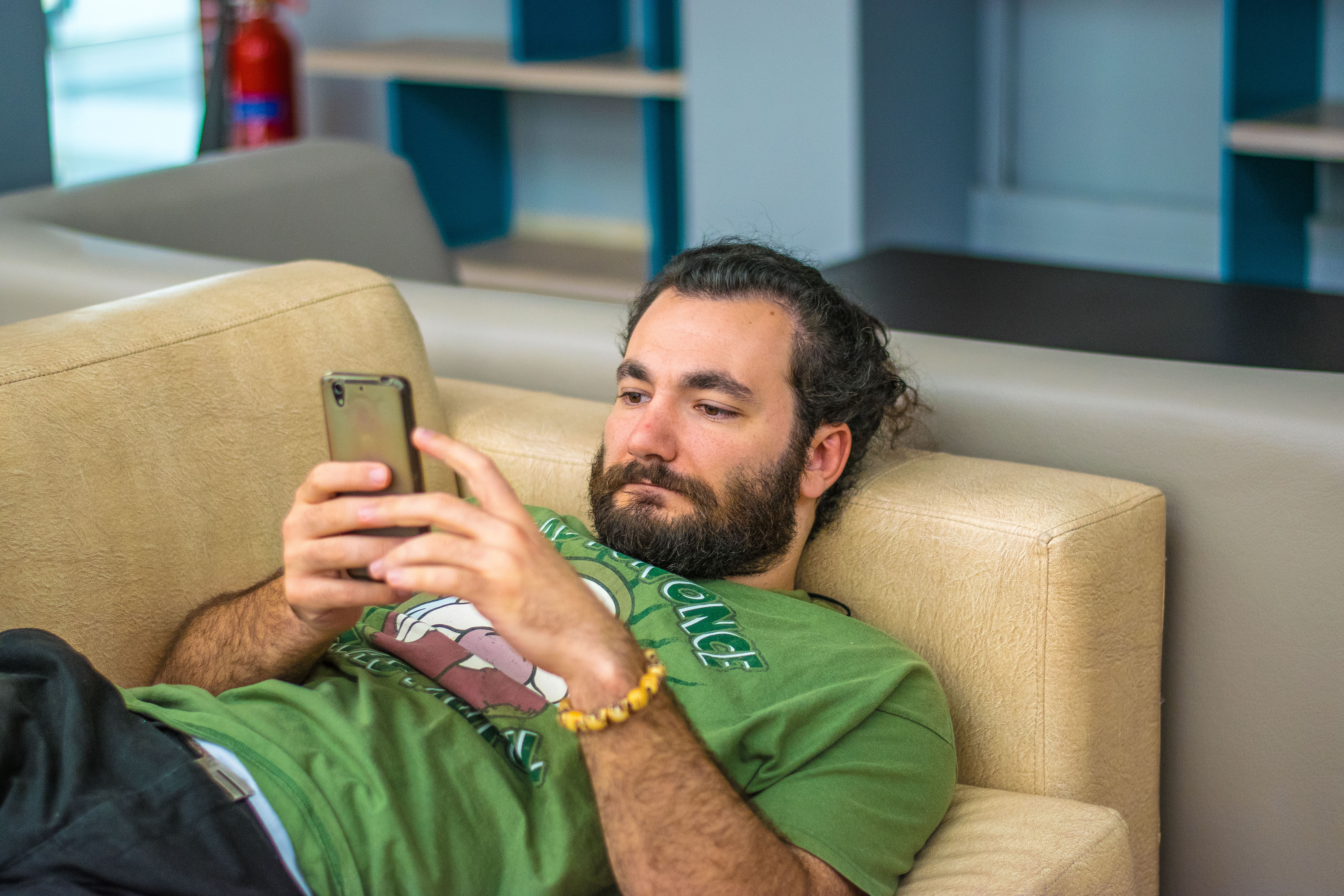 A man with a beard reclines on a couch, focused on his phone, contrasting with a simple trick for a changed life.