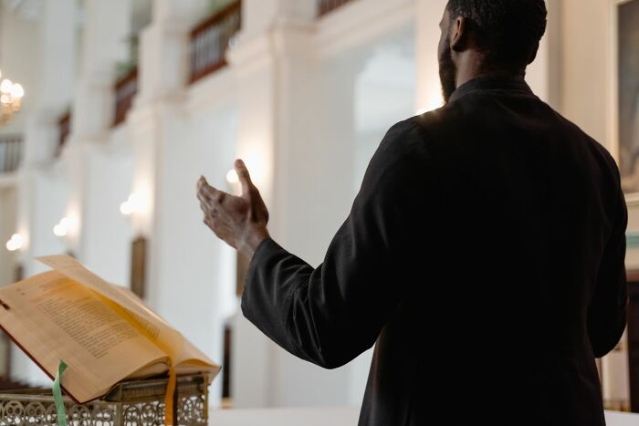 A person in black attire stands with hands raised in a church, possibly feeling deeply evil instincts.
