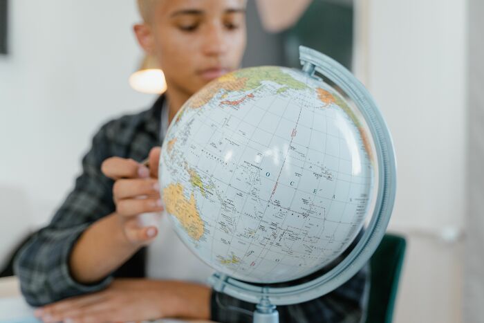 A young geography expert looks closely at a globe, studying the world map to answer quiz questions. A young geography expert looks closely at a globe, studying the world map to answer quiz questions.