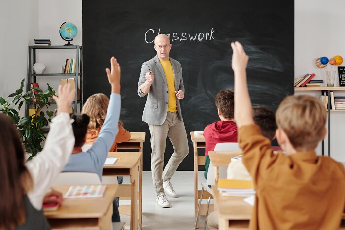 Teacher in front of a class, students raising hands, discussing industry secrets and jobs.