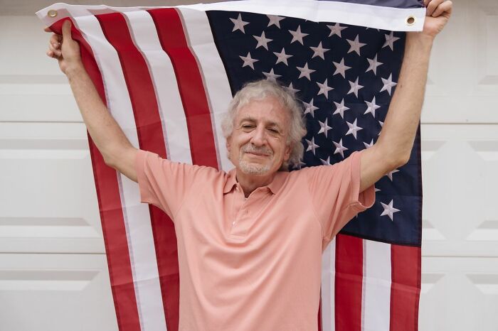 A man smiling and holding an American flag, showcasing American habits.