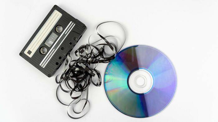 A tangled cassette tape and a shiny CD on a white background, representing 80s and 90s music for a quiz. A tangled cassette tape and a shiny CD on a white background, representing 80s and 90s music for a quiz.