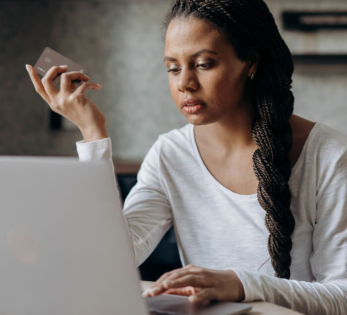 A woman looking at her laptop while holding a credit card, related to child support court backfiring. A woman looking at her laptop while holding a credit card, related to child support court backfiring.