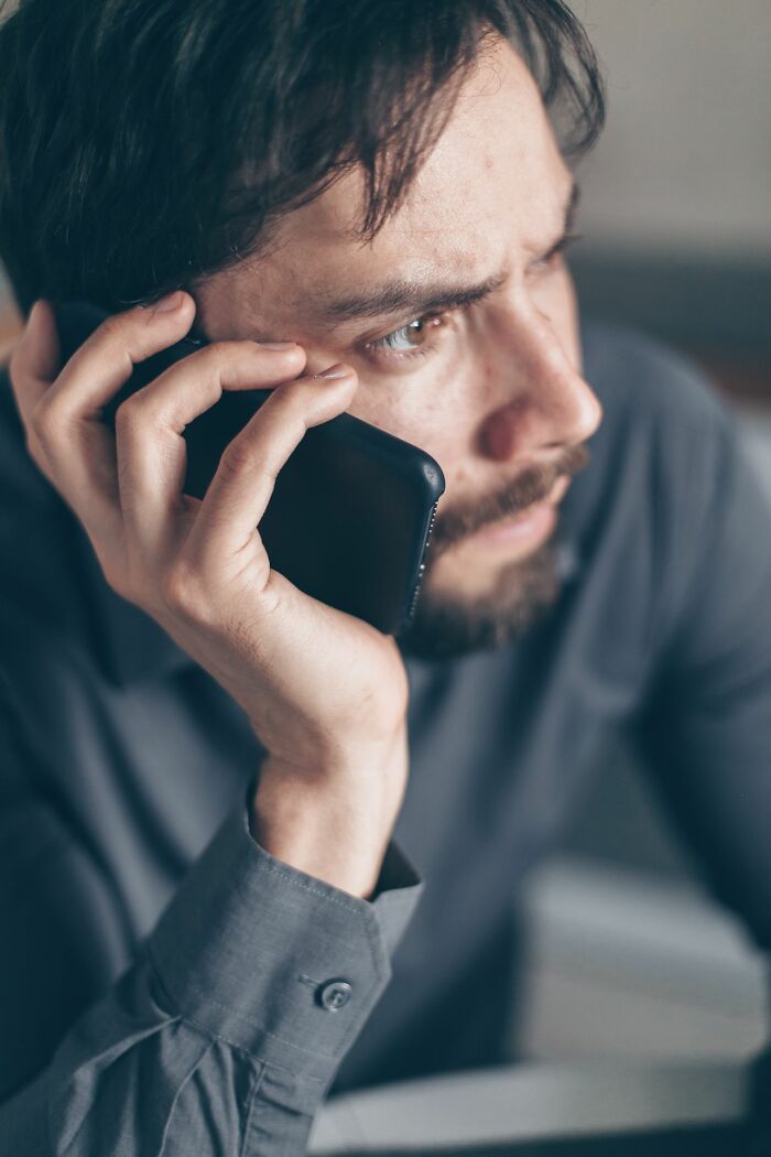 A man with a beard on the phone, looking concerned, perhaps dealing with entitled friends.