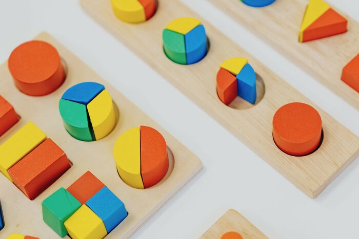 A close-up of colorful wooden math puzzles on a light wood board, featuring geometric shapes like circles, squares, and triangles. A close-up of colorful wooden math puzzles on a light wood board, featuring geometric shapes like circles, squares, and triangles.