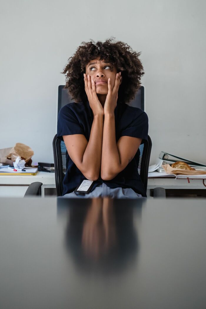 Distressed woman at a desk looking up, hands on face, feeling deeply evil and overwhelmed.