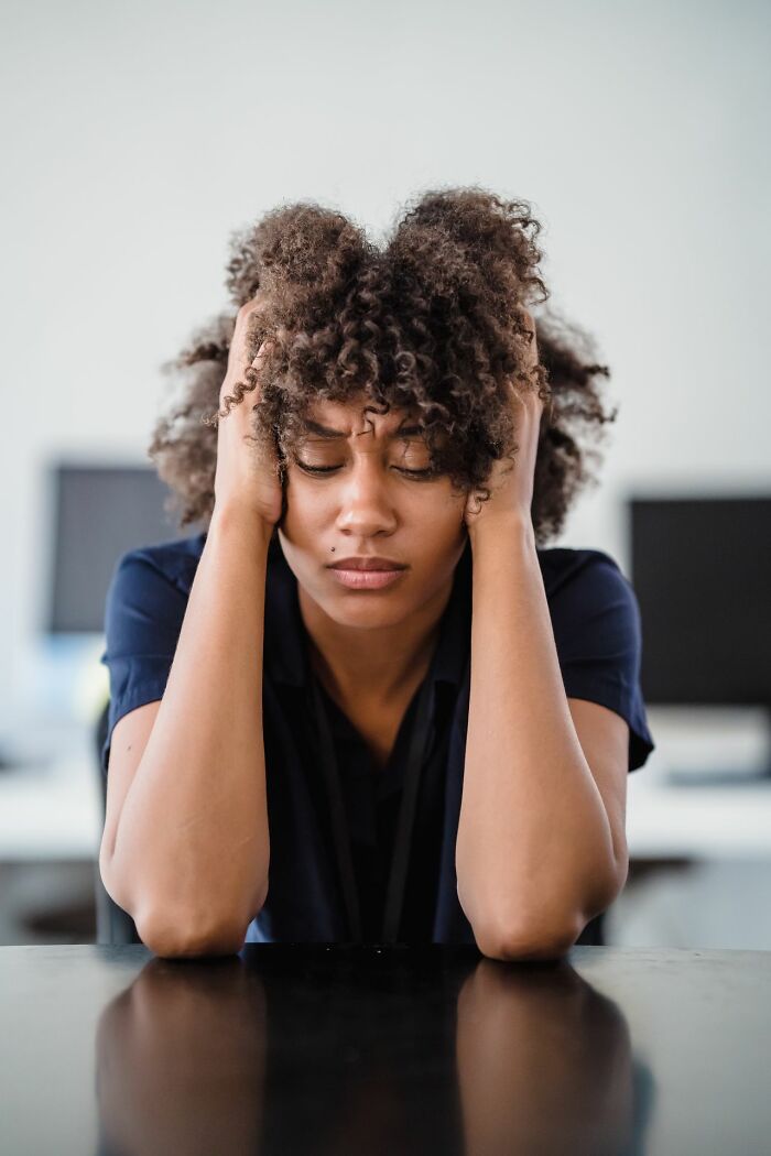 A woman with curly hair holding her head in distress, reflecting the impact of entitled friends.