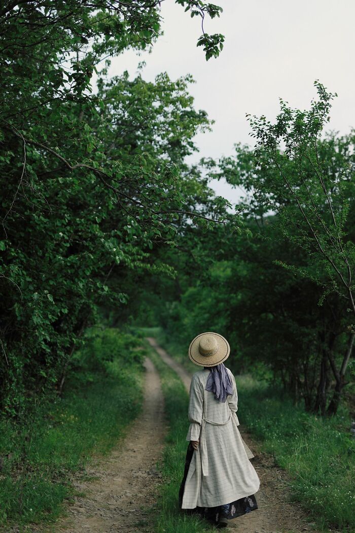 A person in a straw hat walking down a dirt path surrounded by lush green trees, showcasing an unusual way people lost lives.