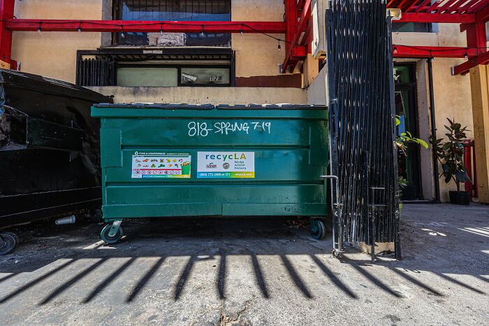 A green dumpster outside a building with health inspections failures.
