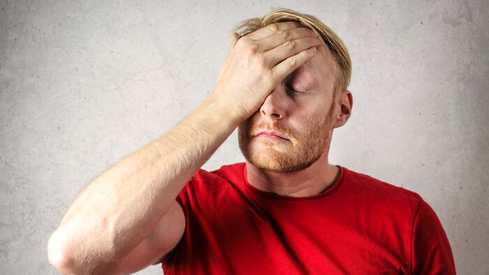 A man with blonde hair and a beard wearing a red shirt, covering his eyes with his hand, looking annoyed at tricky questions. A man with blonde hair and a beard wearing a red shirt, covering his eyes with his hand, looking annoyed at tricky questions.