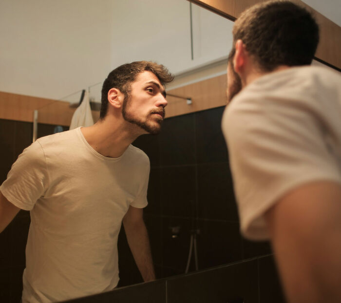 A lonely man with a beard looking intently at his reflection in a bathroom mirror. A lonely man with a beard looking intently at his reflection in a bathroom mirror.
