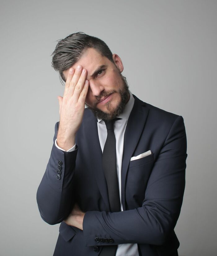 A man in a suit with his hand on his forehead, looking frustrated by ridiculous HR problems.