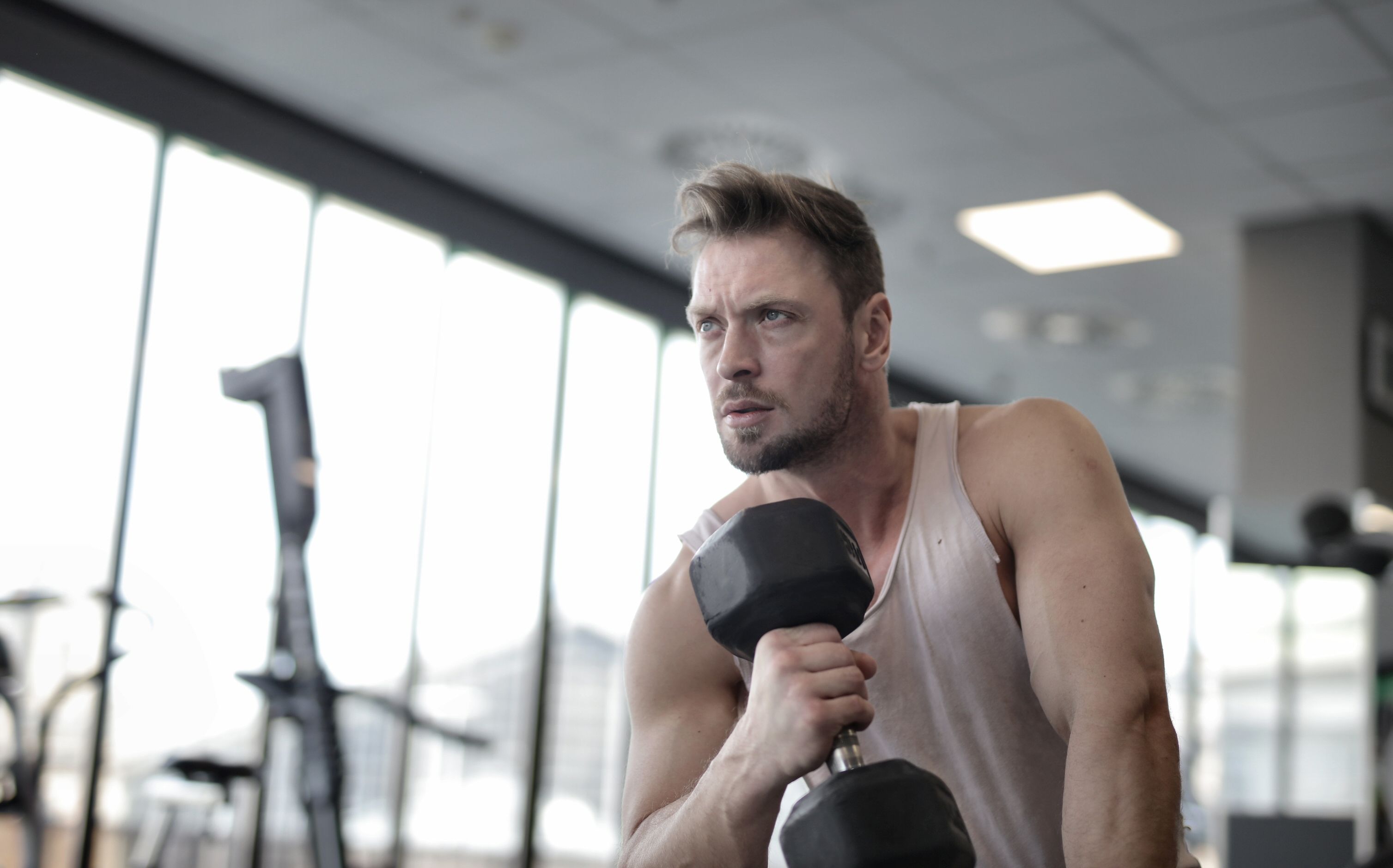 A man with a serious expression lifts a dumbbell in a gym, demonstrating a simple trick for a changed life.