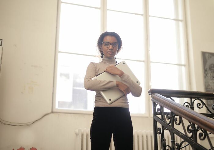A woman in glasses holding a laptop, looking serious, dealing with entitled friends.