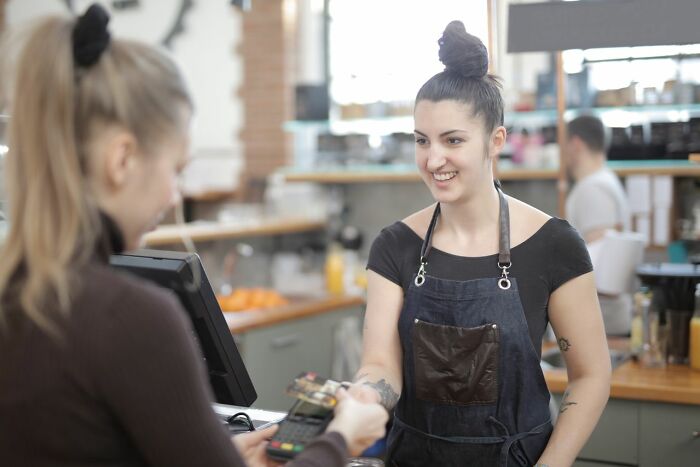 A smiling barista accepting payment from a customer, depicting one of the rarest things that have happened.