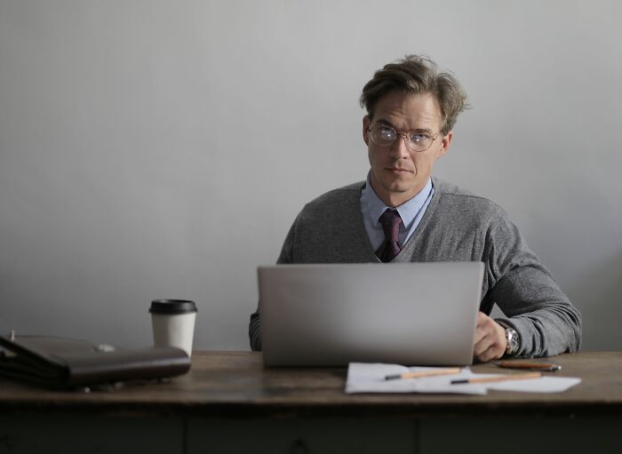 A man in glasses looking intently at the camera while working on a laptop, a professional office story.