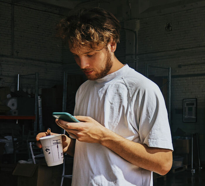 A man engrossed in his phone with a coffee cup, illustrating a common scene in modern dating. A man engrossed in his phone with a coffee cup, illustrating a common scene in modern dating.