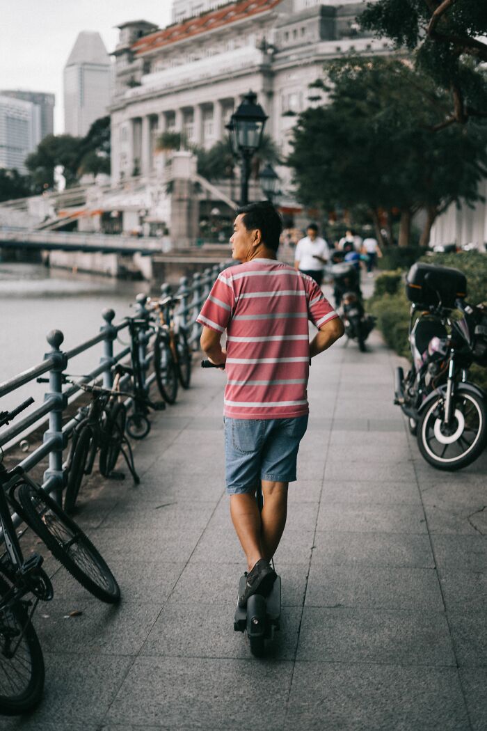 A man on an electric unicycle passes parked bicycles by a river, representing interactions that may lead to misunderstandings between locals and foreigners.