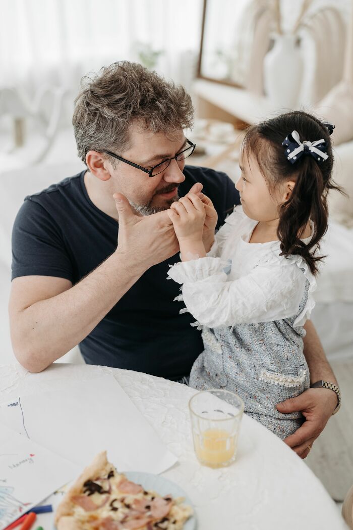 A father gently holds his daughter's hands, showing the bond between parents and children.