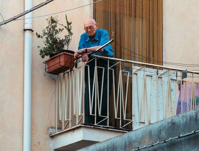 An elderly man in sunglasses on a balcony, looking out, like he's experiencing a public horror story.