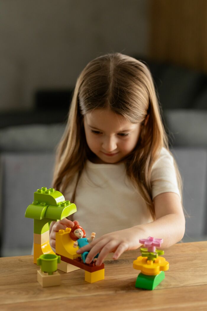 A little girl playing with building blocks and dolls, an innocent moment before parents were terrified.