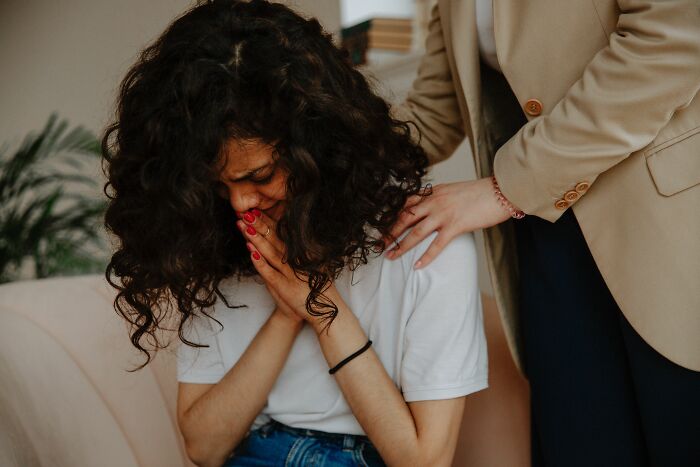 A person with curly hair crying, comforted by another, portraying an emotional final day at work office story.