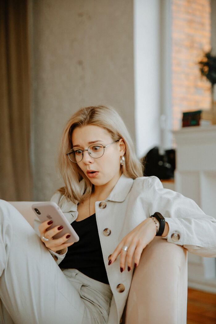 A woman with glasses looking shocked at her phone, depicting the surprise of entitled friends' true colors.