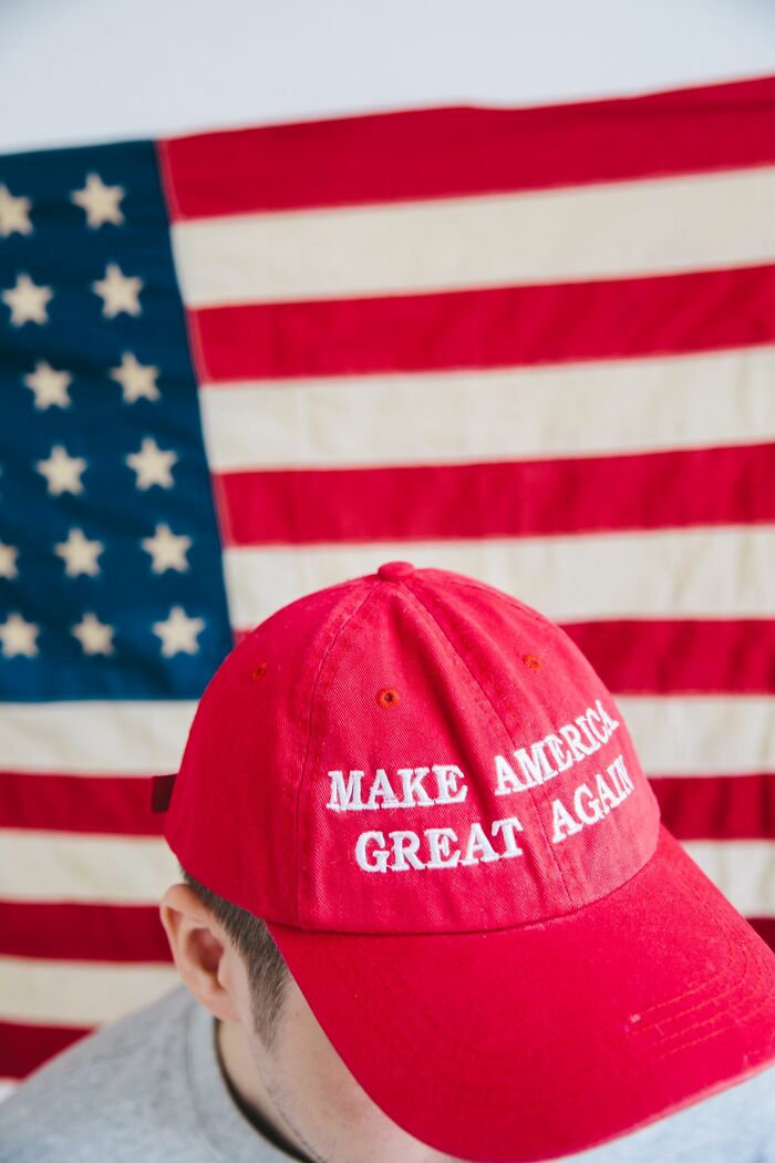 A person wearing a red MAKE AMERICA GREAT AGAIN hat with an American flag in the background, representing secrets.