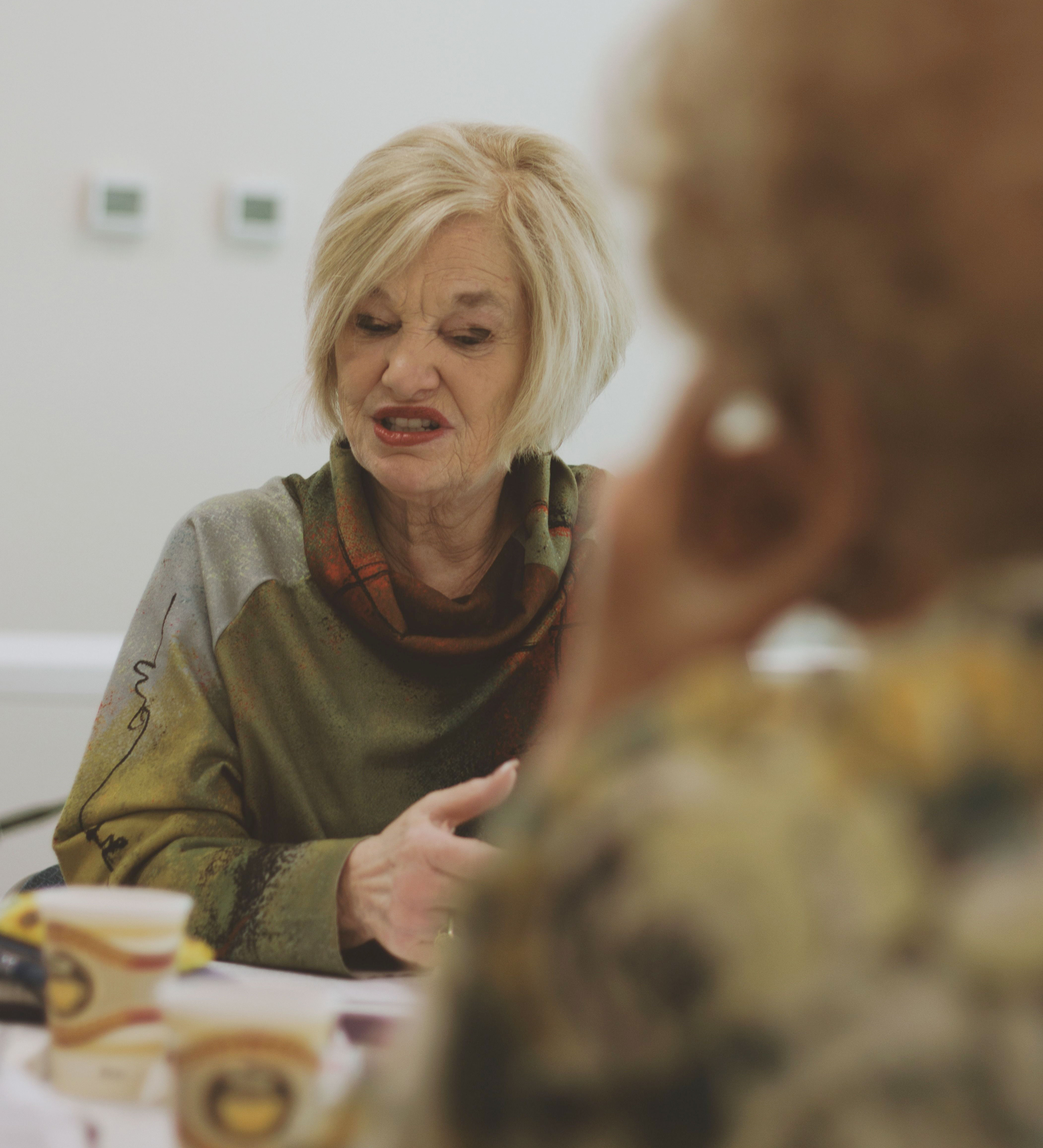 Elderly woman gossiping, making horrible comments, seen with a concerned expression during a conversation.