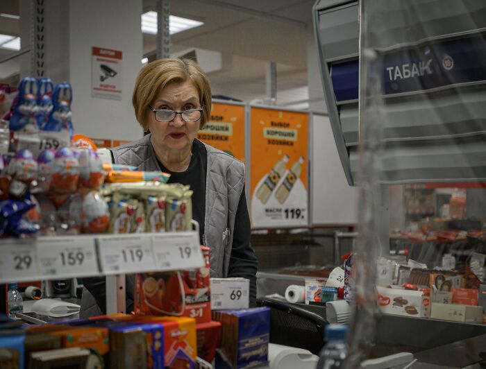 A woman with glasses is behind a counter at a store, part of a crazy office story.