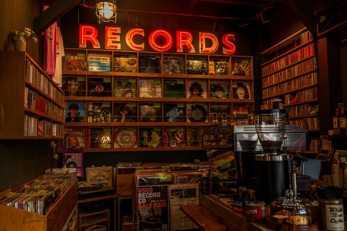 A warmly lit record store with a neon RECORDS sign, showcasing a wide collection of '70s and '80s songs and albums. A warmly lit record store with a neon RECORDS sign, showcasing a wide collection of '70s and '80s songs and albums.