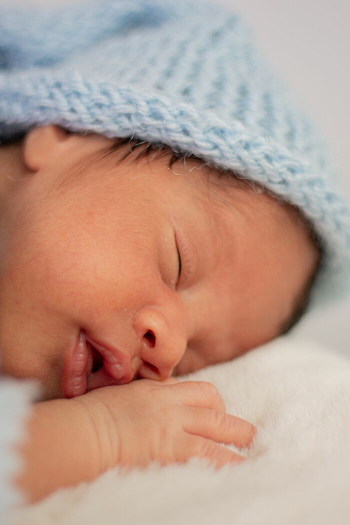 A close-up of a sleeping baby wearing a blue knitted hat, representing the rarest things that can happen.