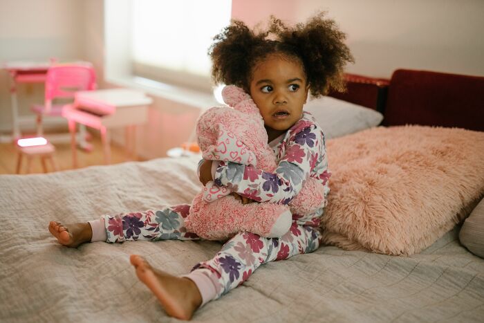A young child in pajamas, clutching a stuffed animal, with a look of worry that could make parents terrified.