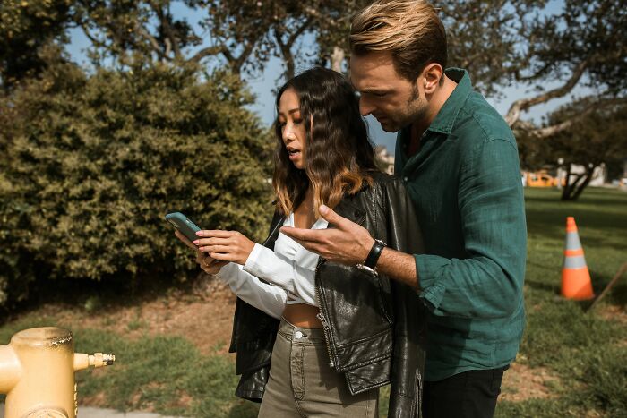 A man looks at a woman's phone, suggesting cheating red flags related to digital secrecy.