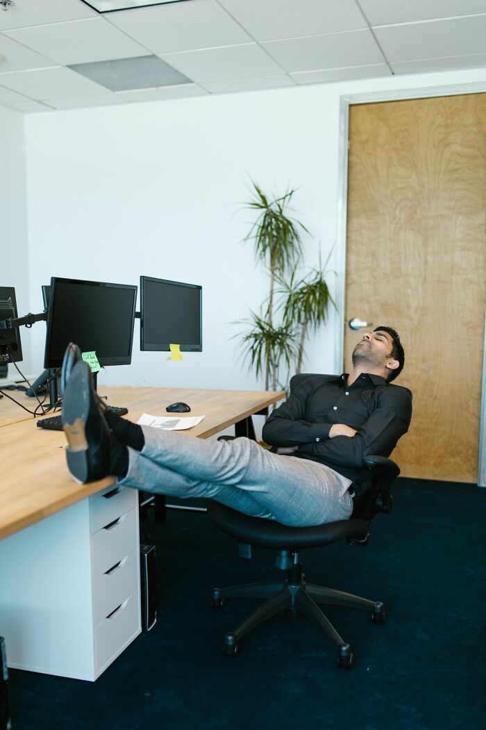 A man in an office chair with his feet on the desk, appearing asleep, related to stereotypically white phrases.
