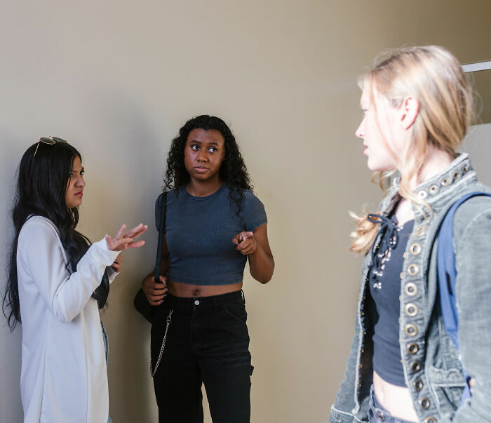 Three young women, one pointing, discussing bullying or mistreating classmate with cancer. Three young women, one pointing, discussing bullying or mistreating classmate with cancer.