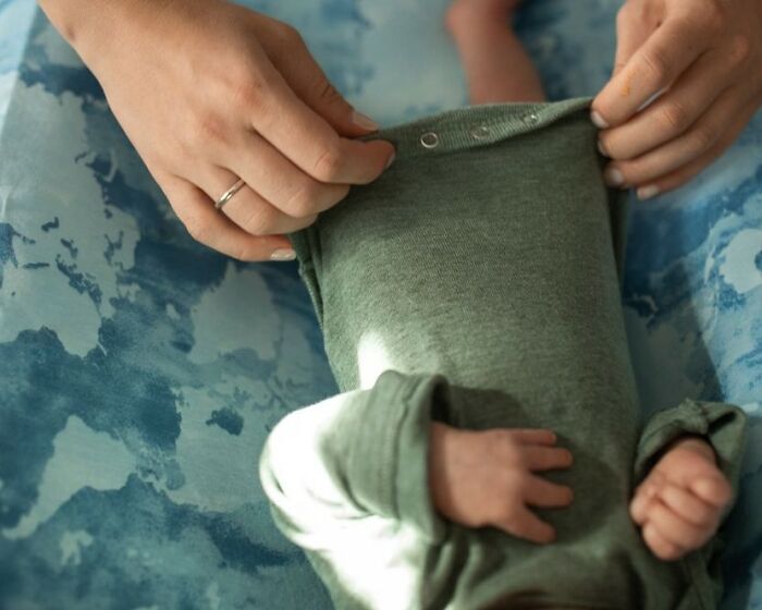 Hands dressing a baby in a green onesie, perhaps relating to public horror stories or daily struggles.