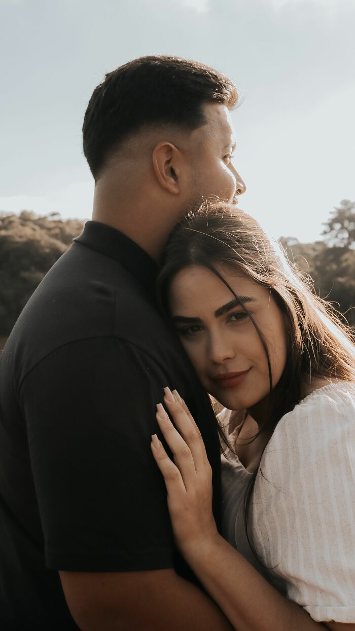 A woman resting her head on a man's shoulder, looking at the camera, showing affection before getting married.